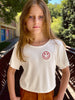 Young girl wearing a white t-shirt with a red smiley face design outdoors.