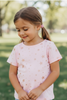Young girl wearing a pink star-patterned shirt standing in a park.