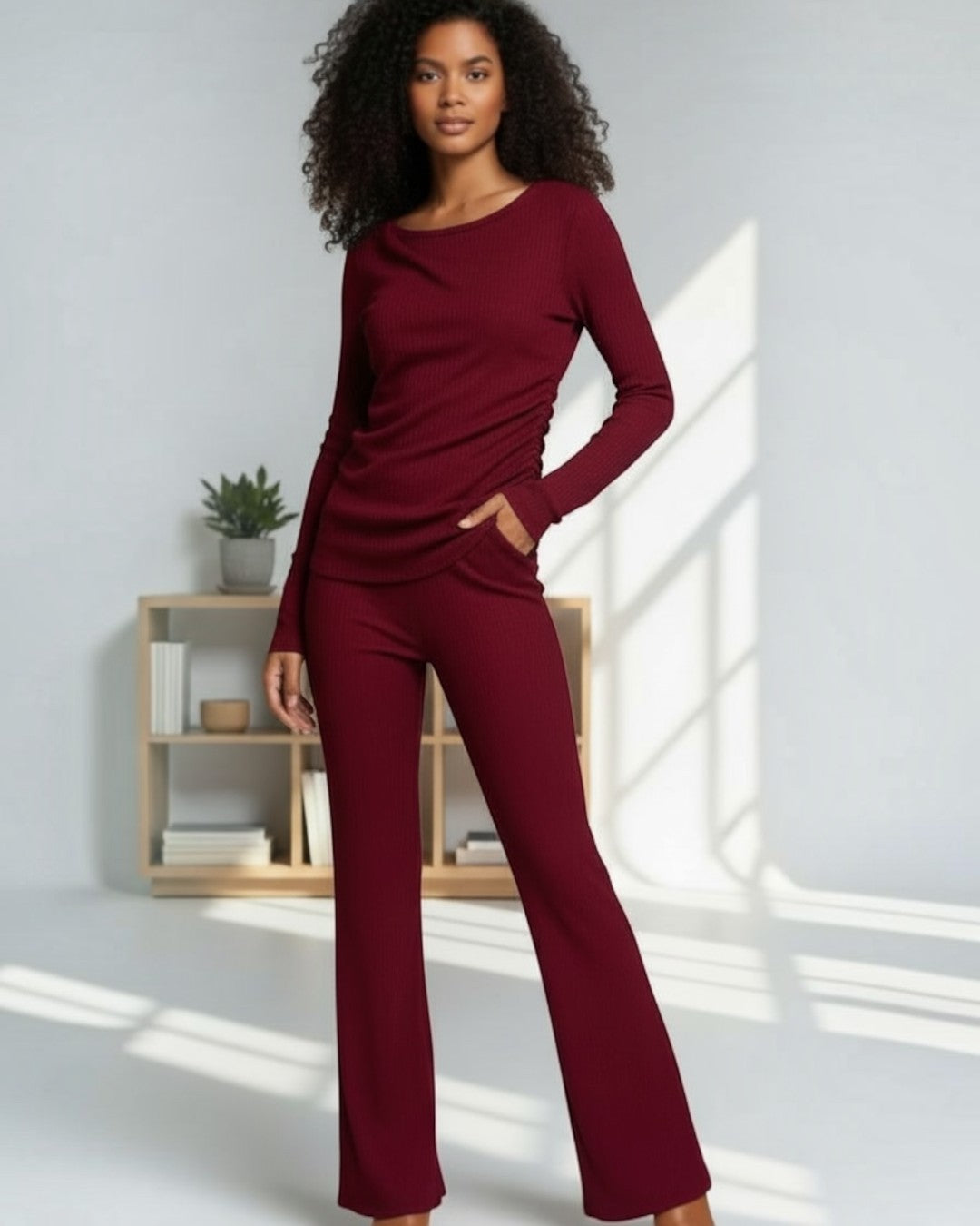 Woman wearing a burgundy outfit standing in a well-lit room with a wooden shelf in the background.