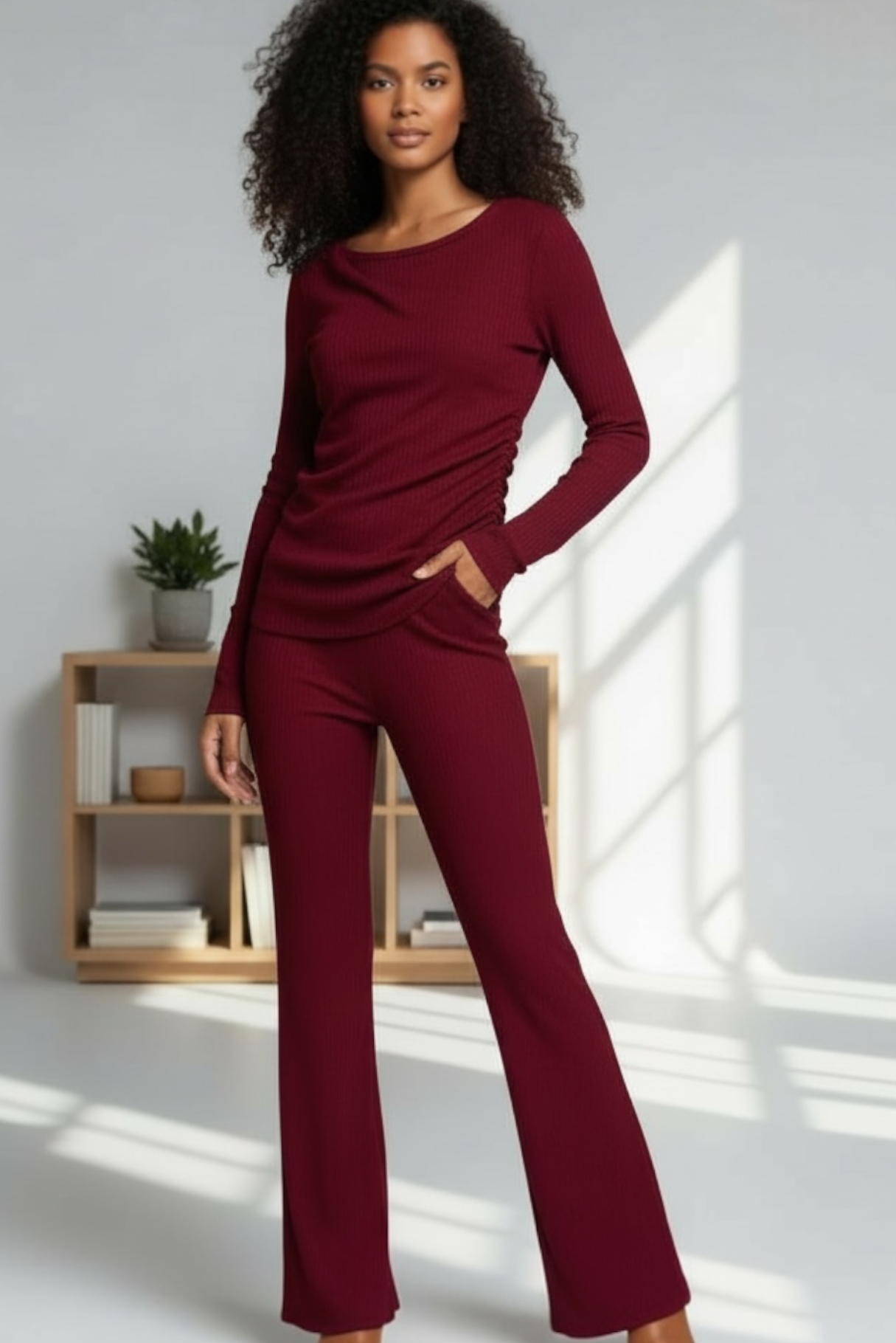 Woman wearing a burgundy outfit standing in a well-lit room with a wooden shelf in the background.