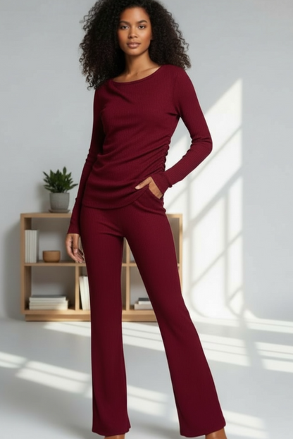 Woman wearing a burgundy outfit standing in a well-lit room with a wooden shelf in the background.
