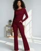 Woman wearing a burgundy outfit standing in a well-lit room with a wooden shelf in the background.