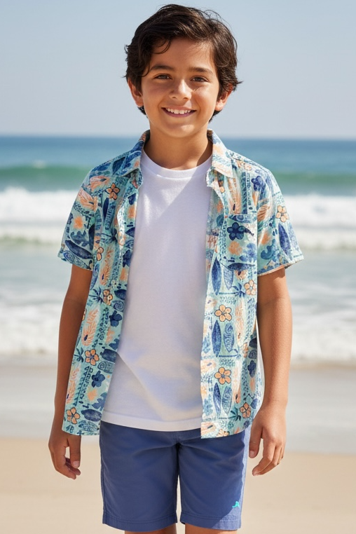 Young boy standing on a beach wearing a colorful shirt and blue shorts.