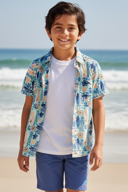Young boy standing on a beach wearing a colorful shirt and blue shorts.