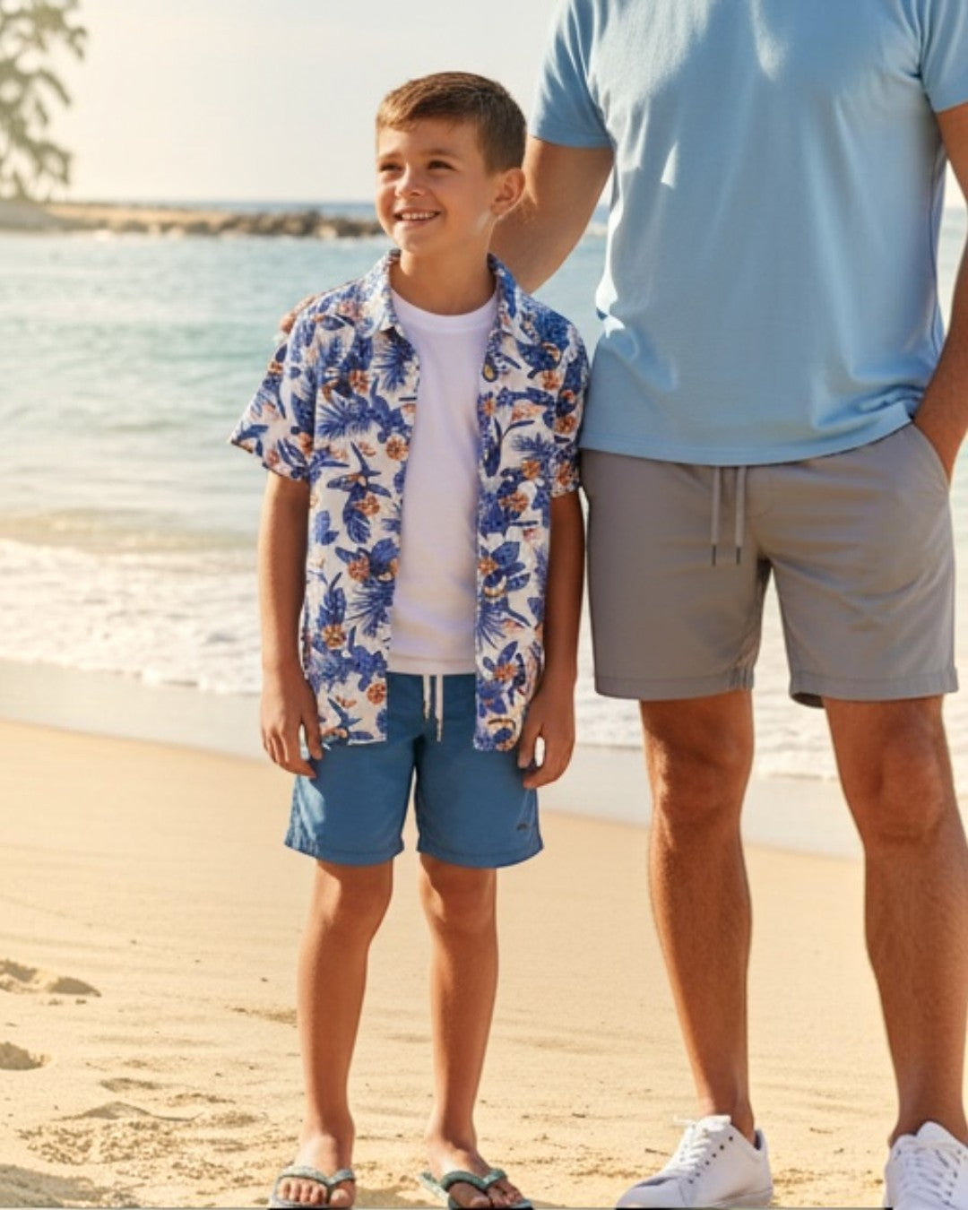 Man and young boy standing on a sandy beach with ocean and palm trees in the background