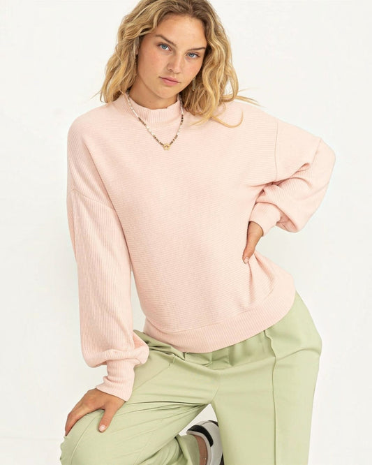 Person wearing a light pink sweater and green pants on a white background