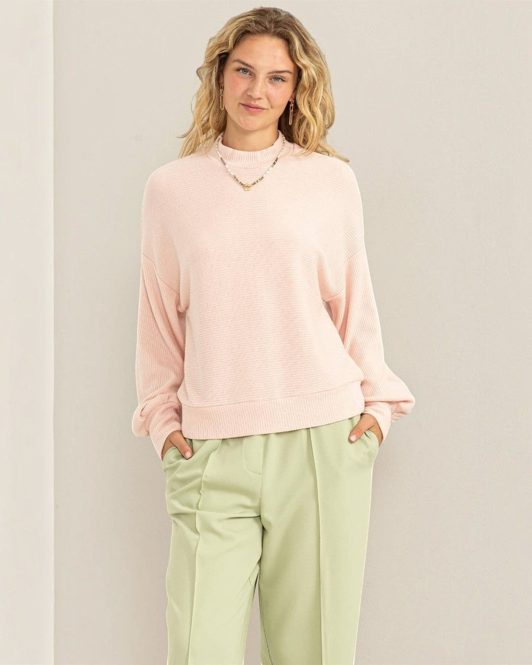 Woman wearing a light pink sweater and light green pants against a beige background