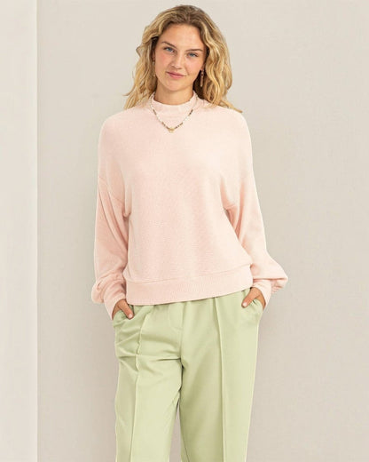 Woman wearing a light pink sweater and light green pants against a beige background