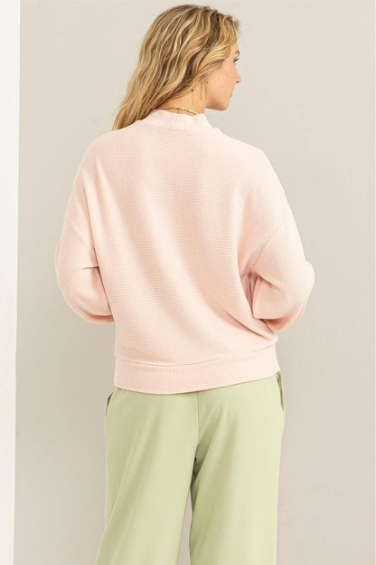 Person wearing a light pink sweater and light green pants against a plain background