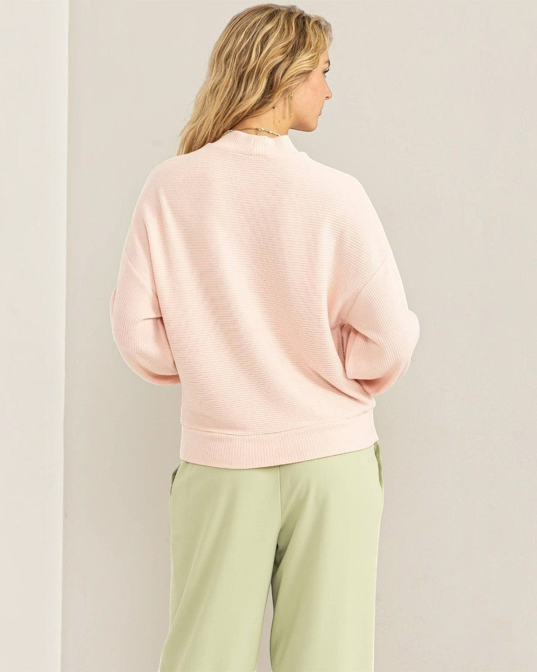 Person wearing a light pink sweater and light green pants against a plain background