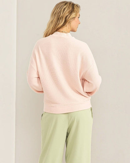 Person wearing a light pink sweater and light green pants against a plain background