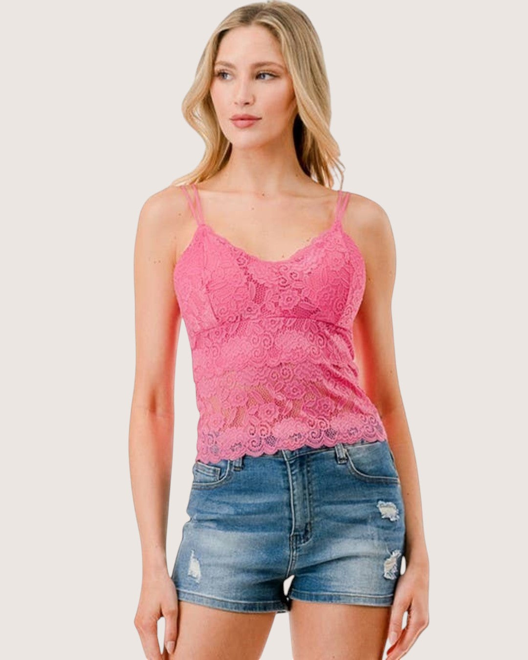 Woman wearing a pink lace tank top and denim shorts on a white background