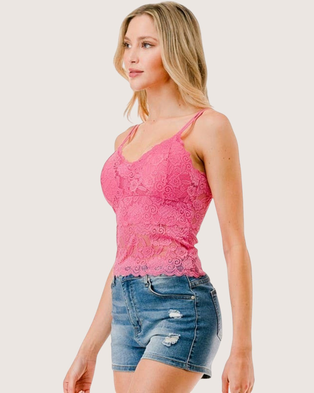 Woman wearing a pink lace tank top and denim shorts on a white background