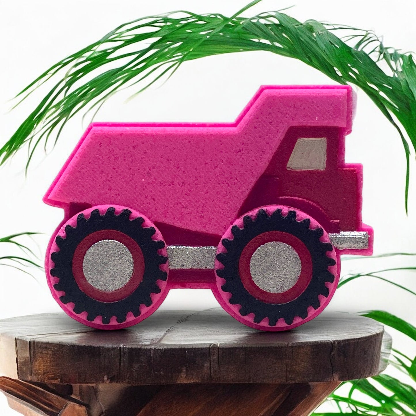 Pink bath bomb truck with black wheels on a wooden surface with green leaves in the background