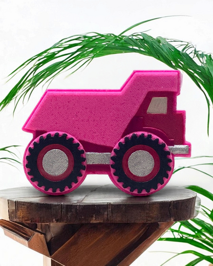 Pink bath bomb truck with black wheels on a wooden surface with green leaves in the background