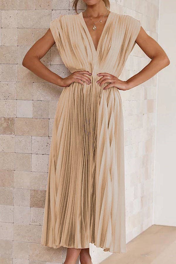 Woman wearing a gold pleated dress against a stone wall.