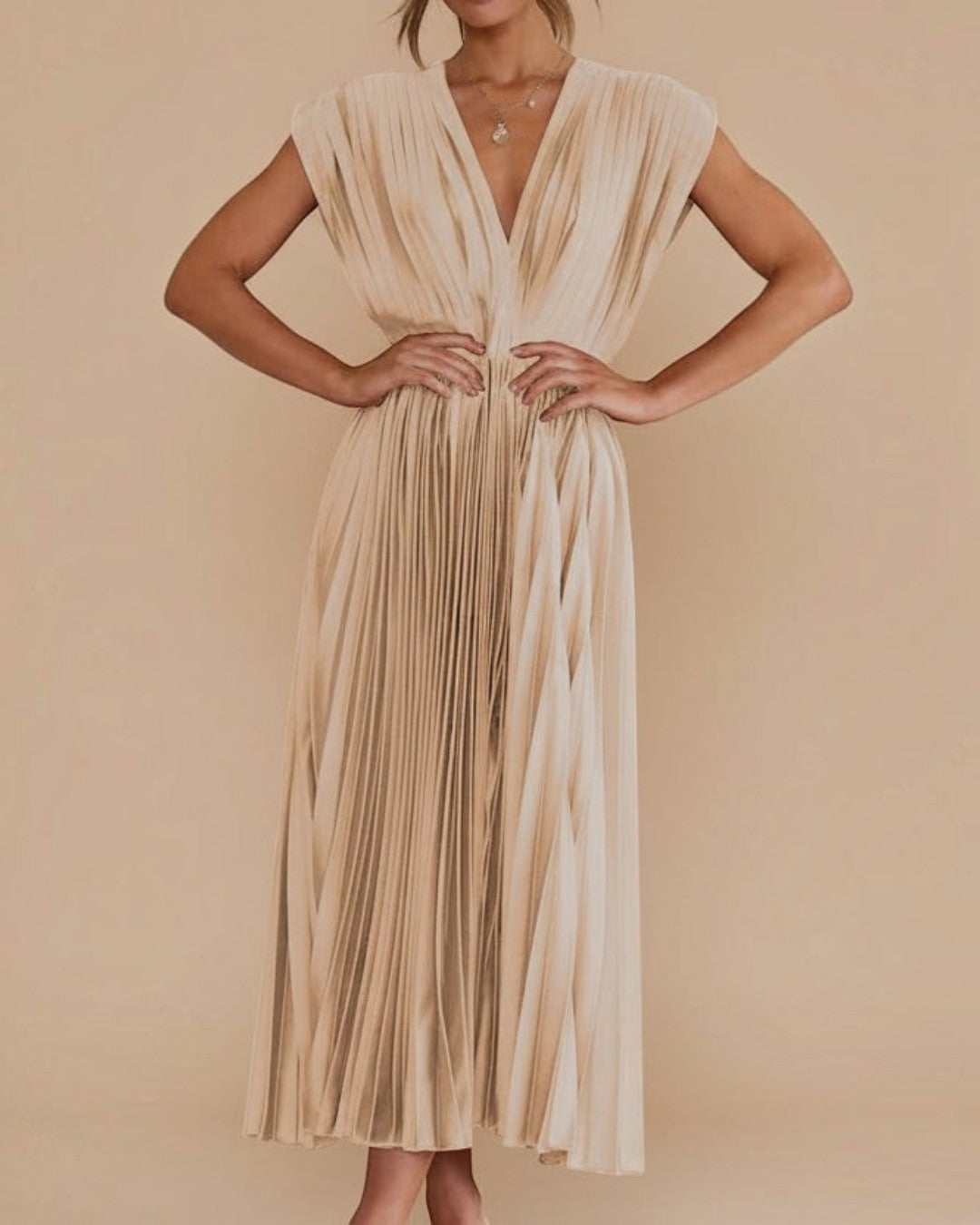 Woman wearing a gold pleated dress against a stone wall.