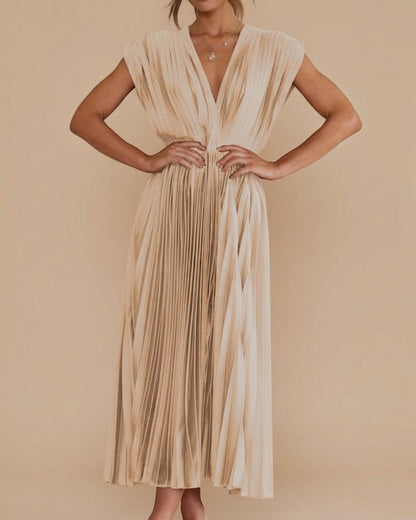 Woman wearing a gold pleated dress against a stone wall.