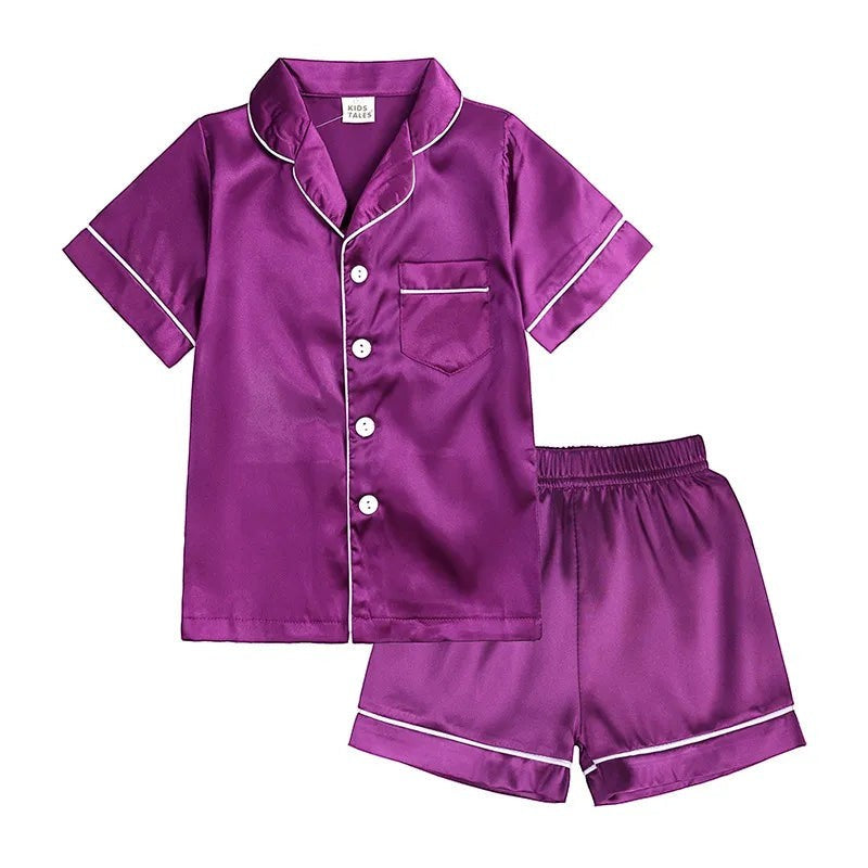 Purple satin pajama set with white buttons and trim on a white background
