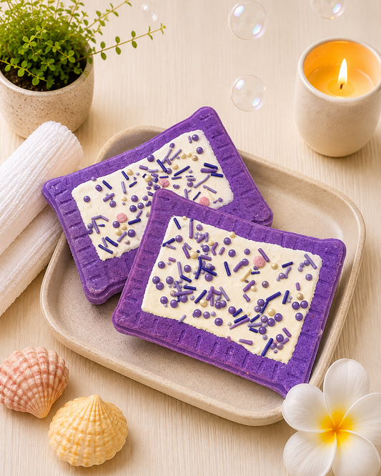 Two purple coasters with white designs on a beige tray, surrounded by decorative items like a candle, plant, and flowers.