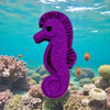 Purple seahorse-shaped toy on a coral reef with fish swimming around
