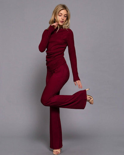 Woman wearing a burgundy dress with flared legs on a gray background