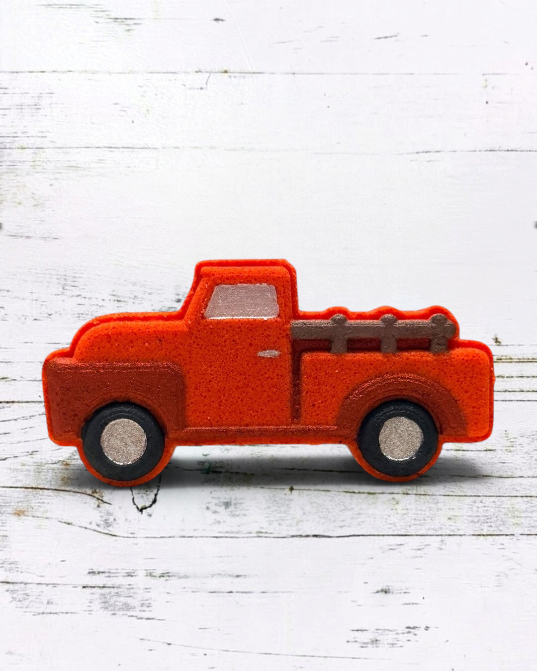 Red bath bomb truck with a wooden bed on a white wooden surface