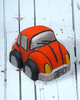 A red orange Volkswagen Bug car-shaped bath bomb with black and yellow accents on a wooden surface with water droplets around it.