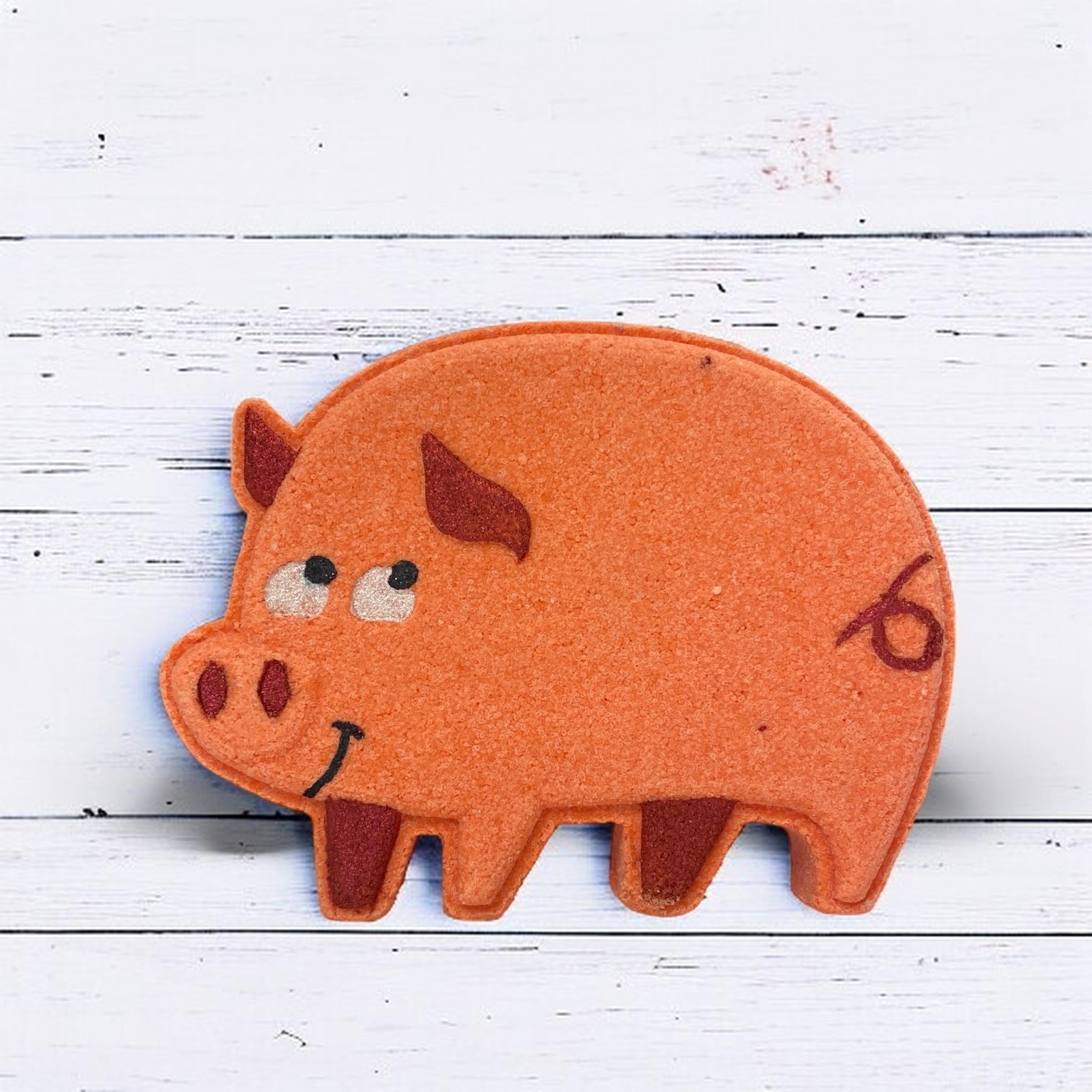 Felt pig-shaped object with a smiley face on a white wooden background