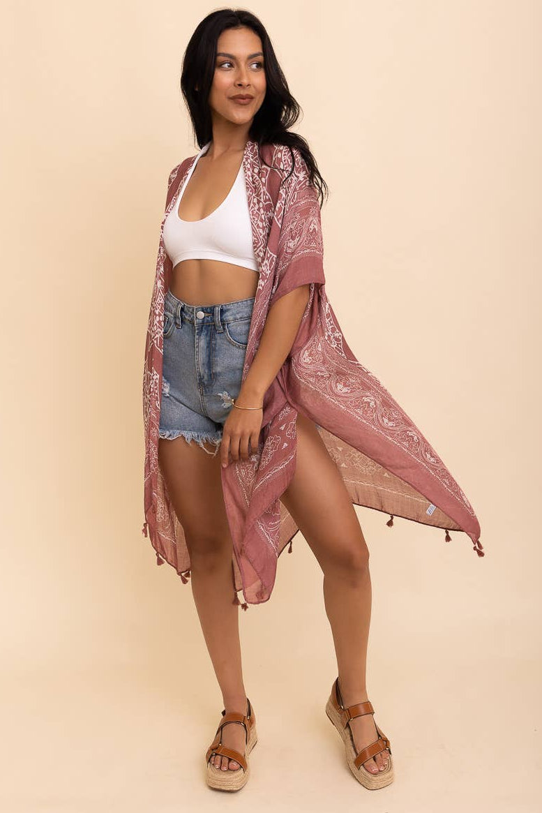 Woman wearing a pink lace kimono over a white top and denim shorts on a beige background
