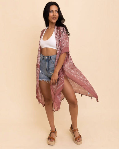 Woman wearing a pink lace kimono over a white top and denim shorts on a beige background