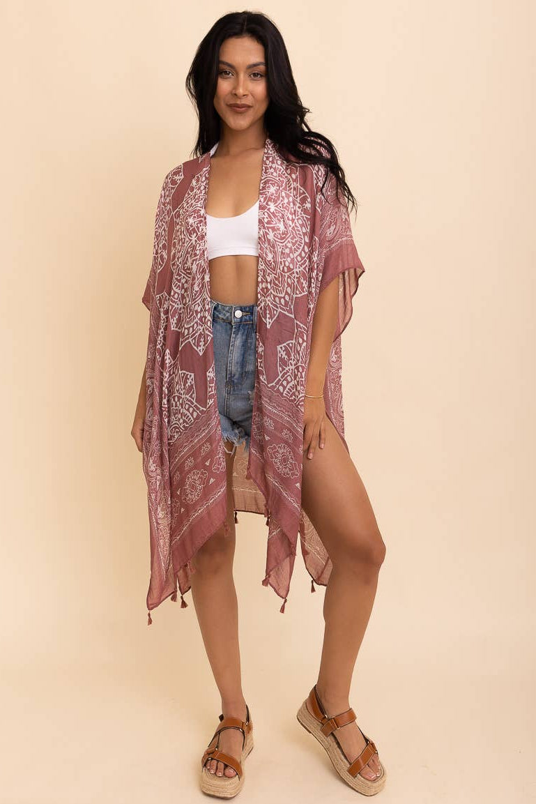 Woman wearing a patterned kimono over a white top and denim shorts on a beige background