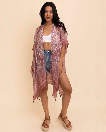 Woman wearing a patterned kimono over a white top and denim shorts on a beige background