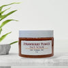 Jar of Strawberry Pumice Face Scrub on a marble surface with a plant in the background