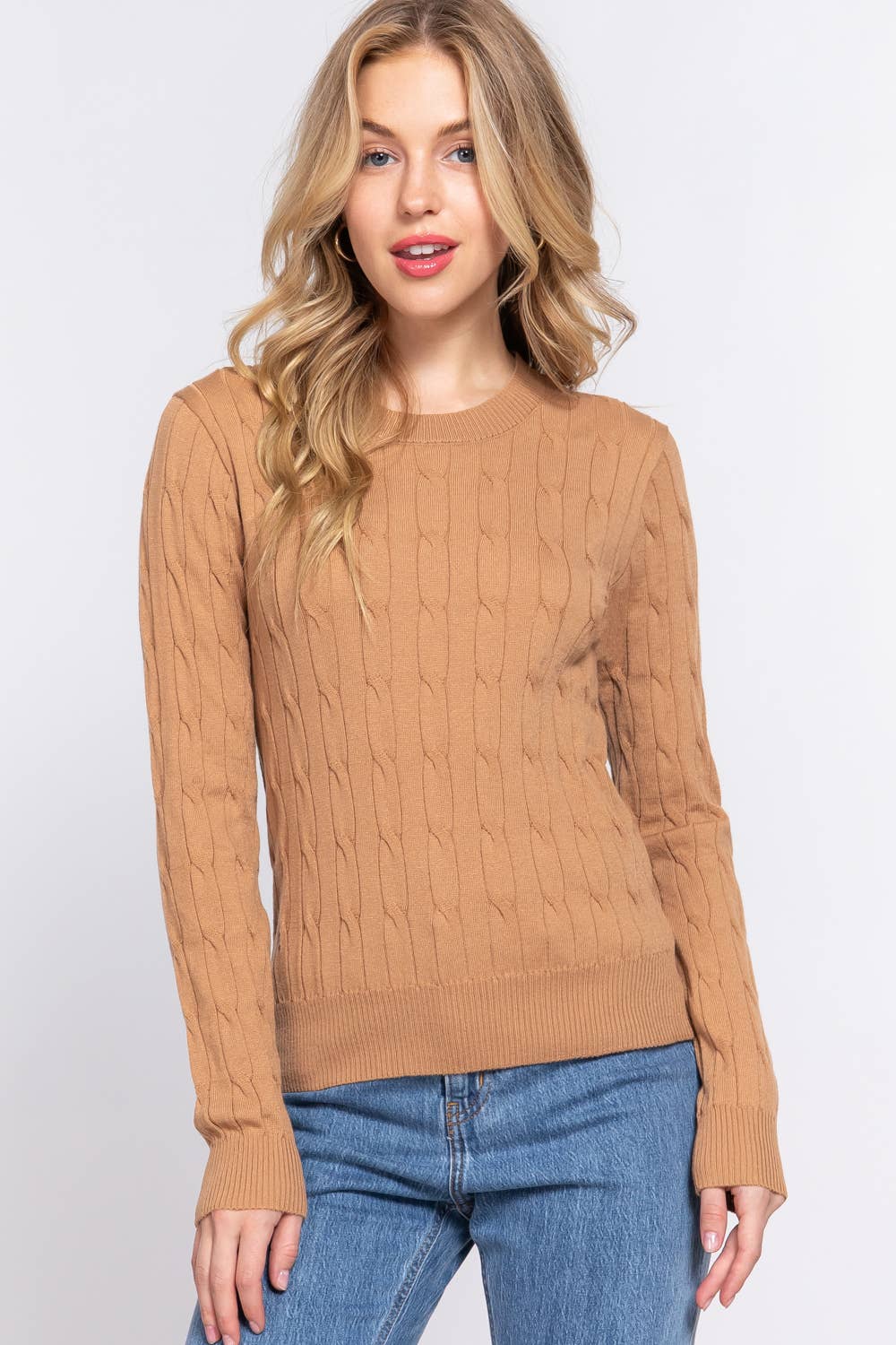 Woman wearing a brown cable knit sweater and blue jeans on a white background