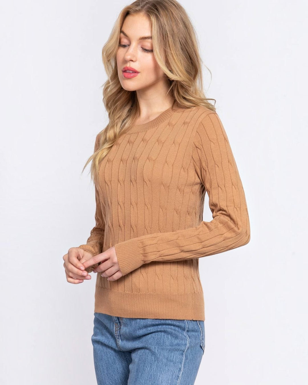 Woman wearing a brown cable knit sweater and blue jeans on a white background