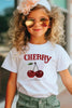 Child wearing a white t-shirt with cherry design and sunglasses outdoors