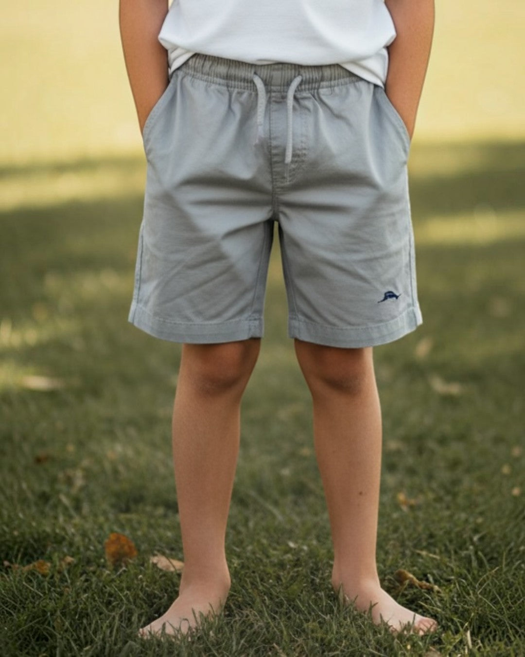 Young boy standing on grass wearing a light blue t-shirt and gray shorts.