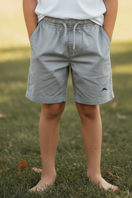 Young boy standing on grass wearing a light blue t-shirt and gray shorts.