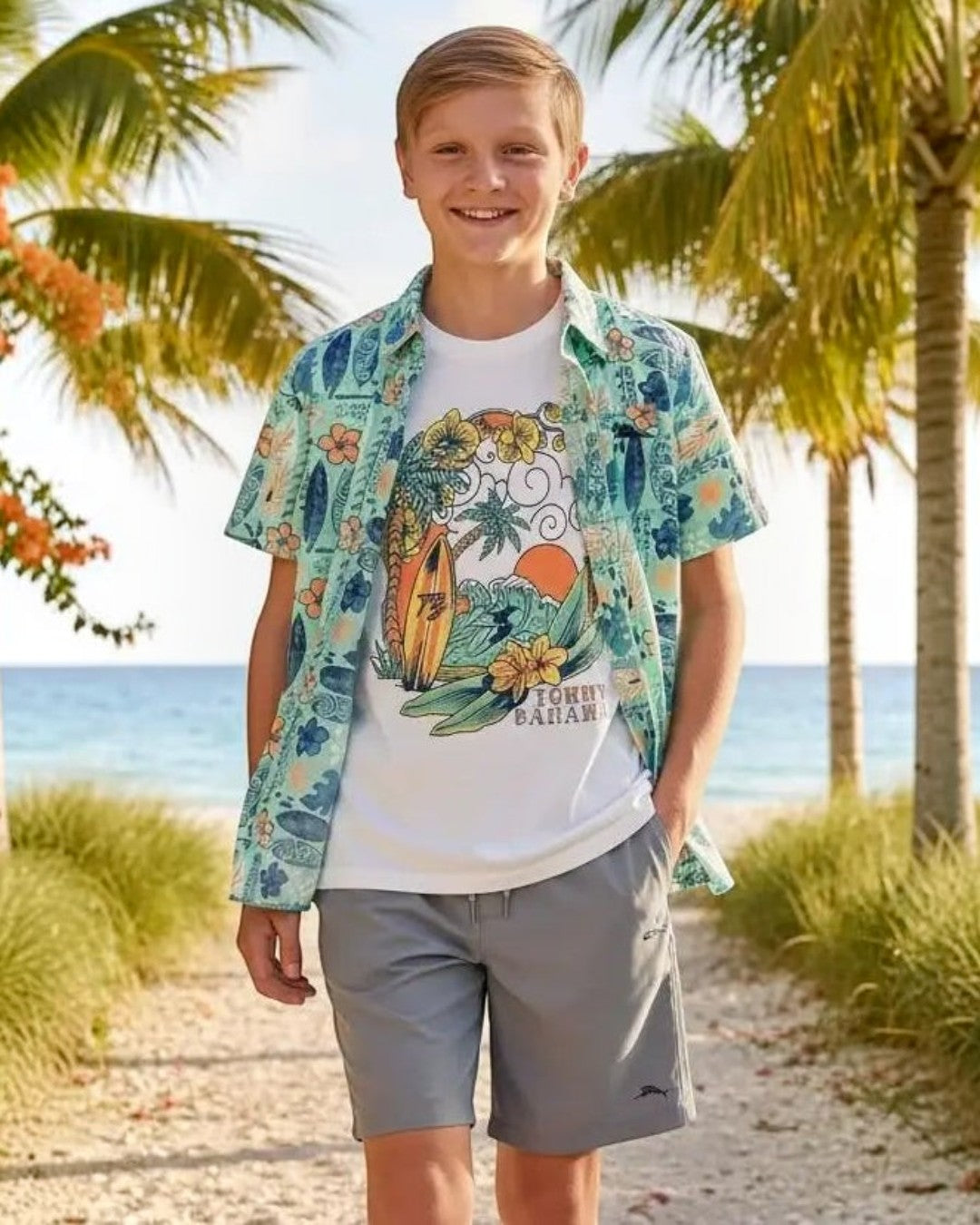 Young boy standing on a beach path with palm trees and ocean in the background