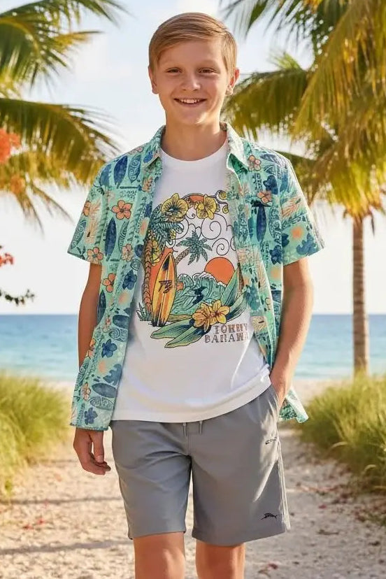 Young boy standing on a beach path with palm trees and ocean in the background