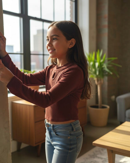 Young girl in a maroon sweater and blue jeans standing indoors with a blurred background
