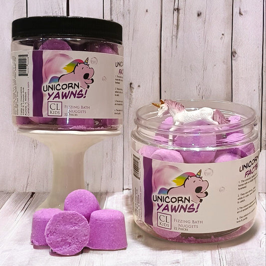 Jar of purple bath fizzies labeled 'Unicorn Yawns' on a wooden surface.