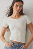 Woman wearing a white ribbed crop top and blue jeans against a plain background