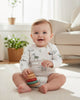 Baby sitting on a carpeted floor holding colorful wooden blocks in a bright living room.