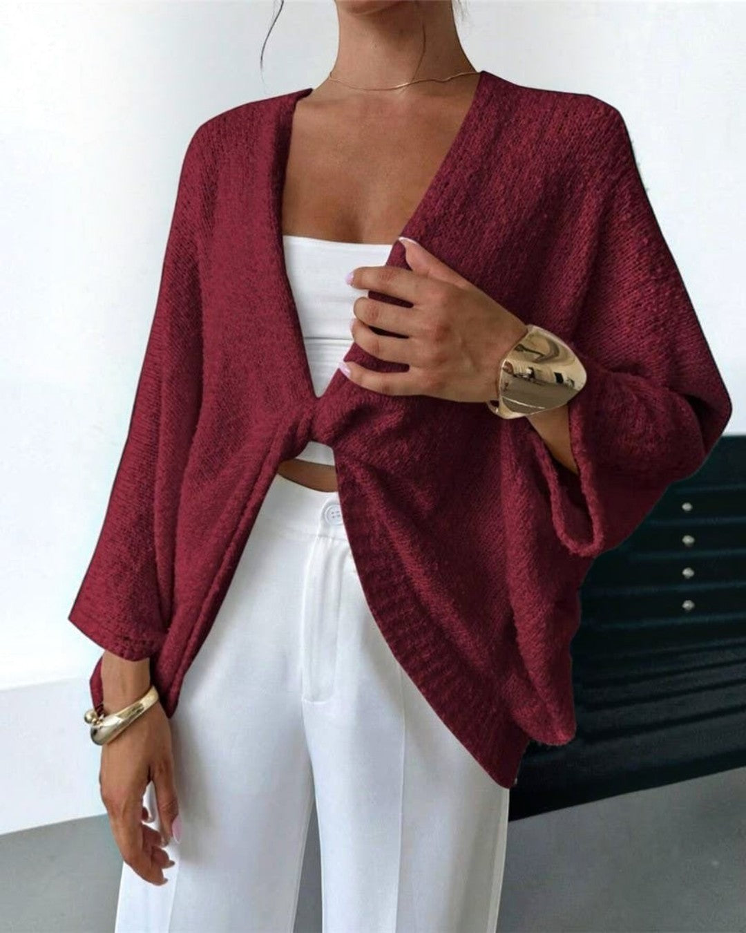 Person wearing a burgundy cardigan over a white top and pants on a plain background