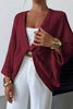 Person wearing a burgundy cardigan over a white top and pants on a plain background