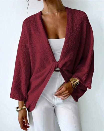 Person wearing a burgundy knitted cardigan over a white top and pants on a plain background