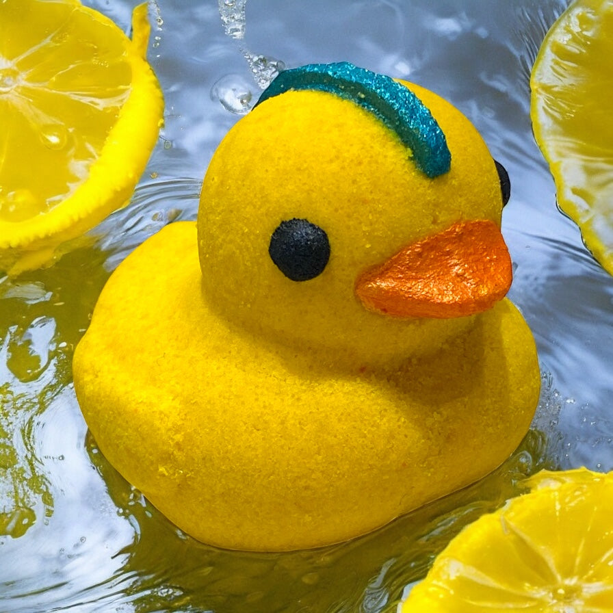 Yellow rubber duck with a blue beak and orange bill floating in water surrounded by lemon slices.