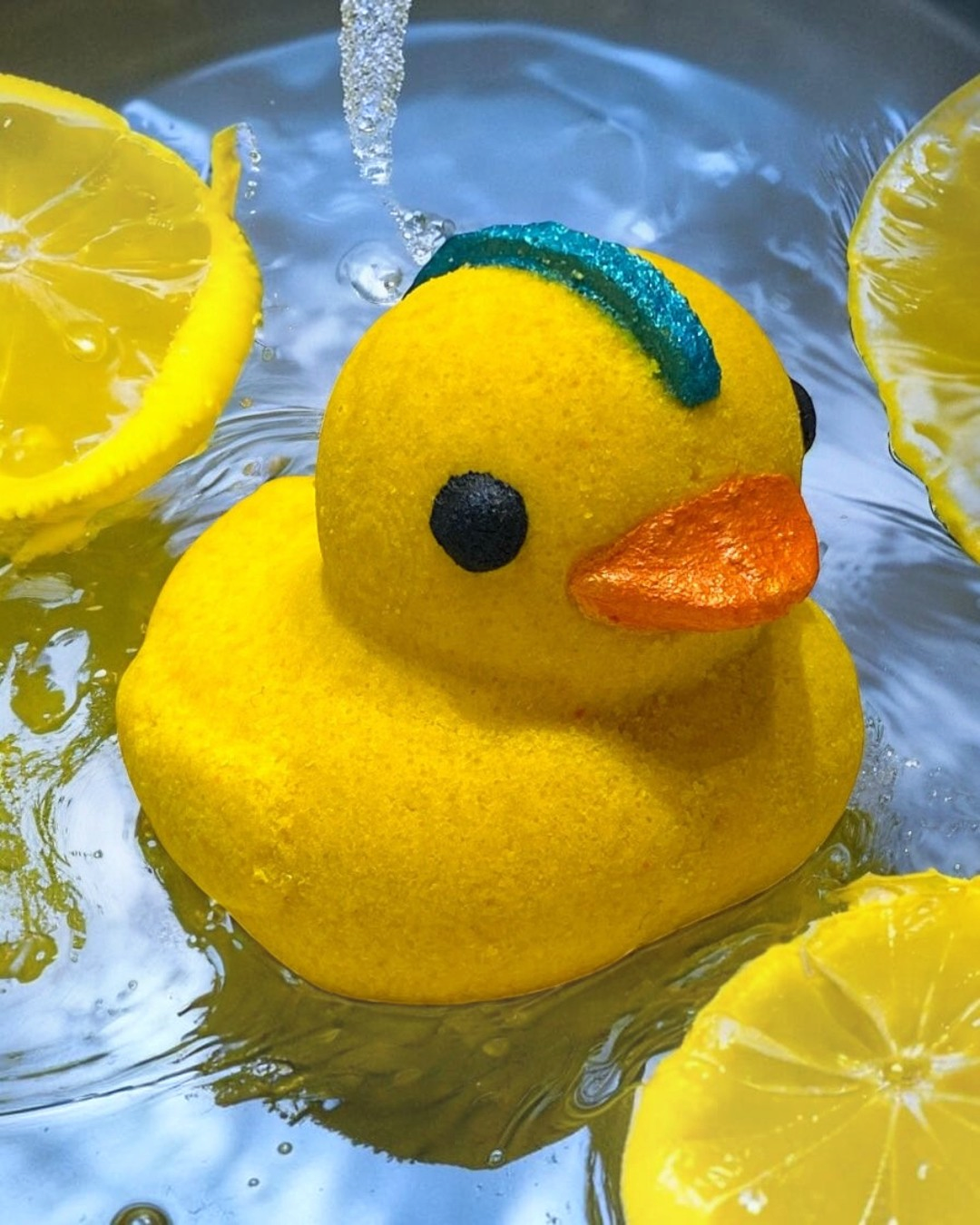 Yellow rubber duck with a blue beak and orange bill floating in water surrounded by lemon slices.